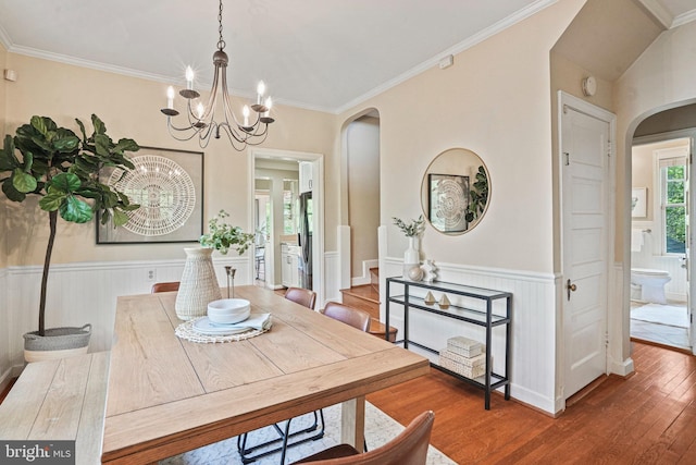 dining area featuring an inviting chandelier, wood-type flooring, arched walkways, a wainscoted wall, and ornamental molding