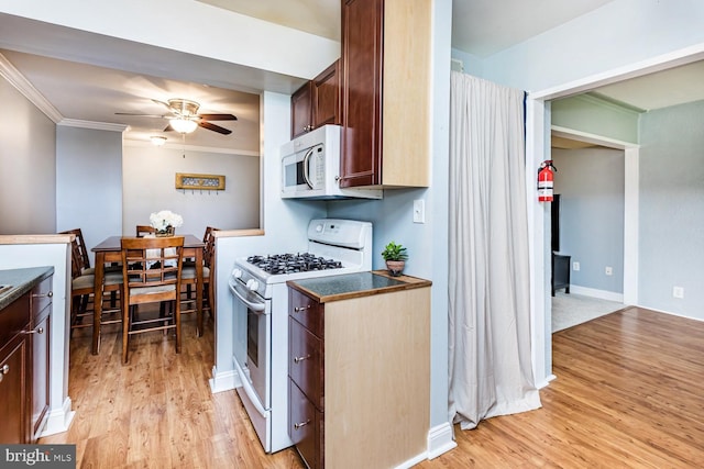 kitchen featuring light wood finished floors, ceiling fan, dark countertops, and white appliances