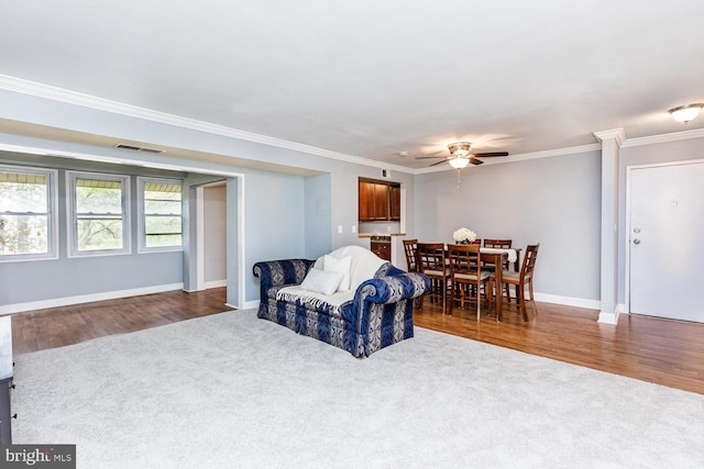 living area with baseboards, ornamental molding, ceiling fan, dark carpet, and dark wood-type flooring