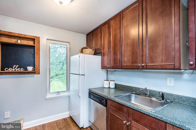 kitchen featuring stainless steel dishwasher, freestanding refrigerator, wood finished floors, a sink, and baseboards