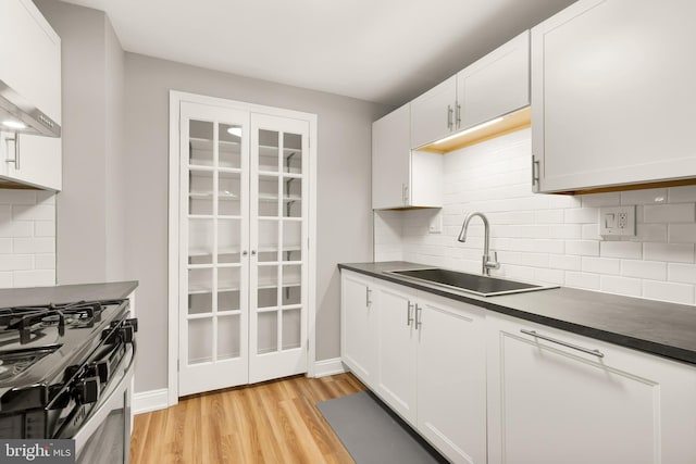 kitchen with dark countertops, white cabinets, light wood-type flooring, and a sink
