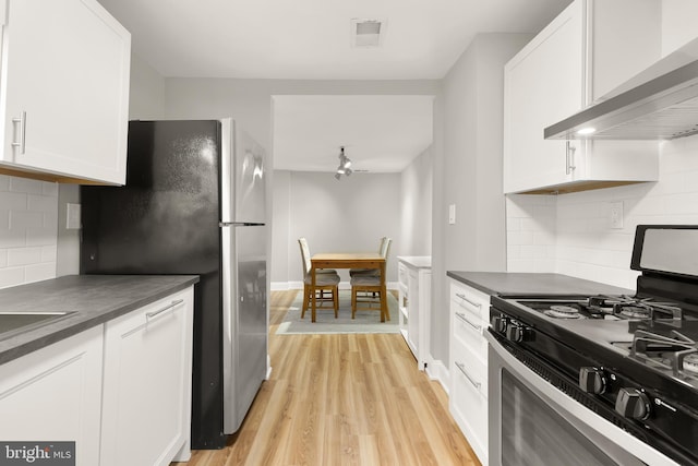 kitchen with dark countertops, light wood finished floors, white cabinets, stainless steel appliances, and wall chimney exhaust hood