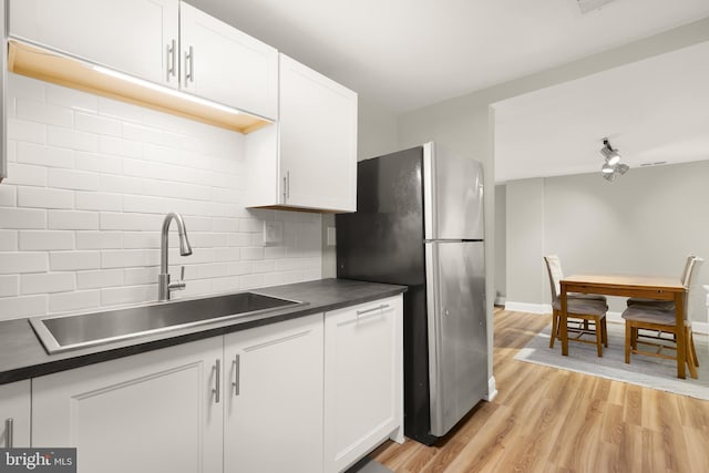 kitchen with a sink, tasteful backsplash, dark countertops, freestanding refrigerator, and light wood-style floors