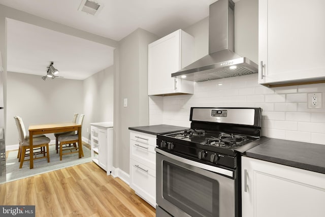 kitchen featuring dark countertops, wall chimney range hood, visible vents, and stainless steel gas range