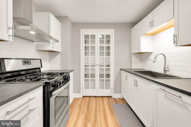 kitchen featuring dark countertops, stainless steel range with gas stovetop, wall chimney exhaust hood, and a sink