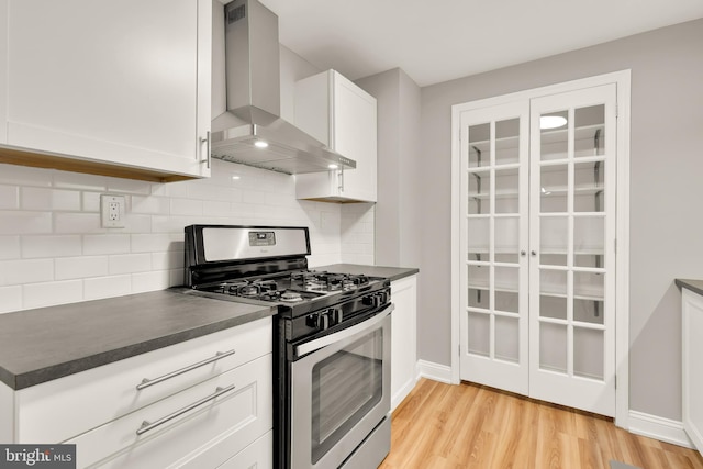 kitchen with light wood-style flooring, dark countertops, white cabinetry, wall chimney exhaust hood, and stainless steel range with gas stovetop