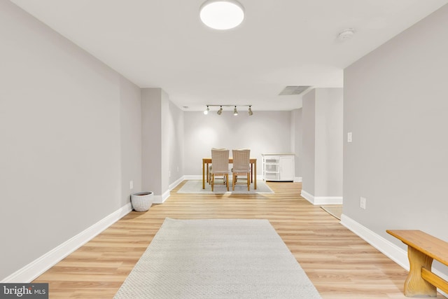 hallway with track lighting, light wood-style flooring, visible vents, and baseboards