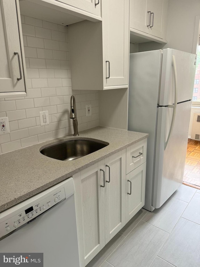 kitchen featuring white appliances, light stone countertops, white cabinetry, a sink, and backsplash