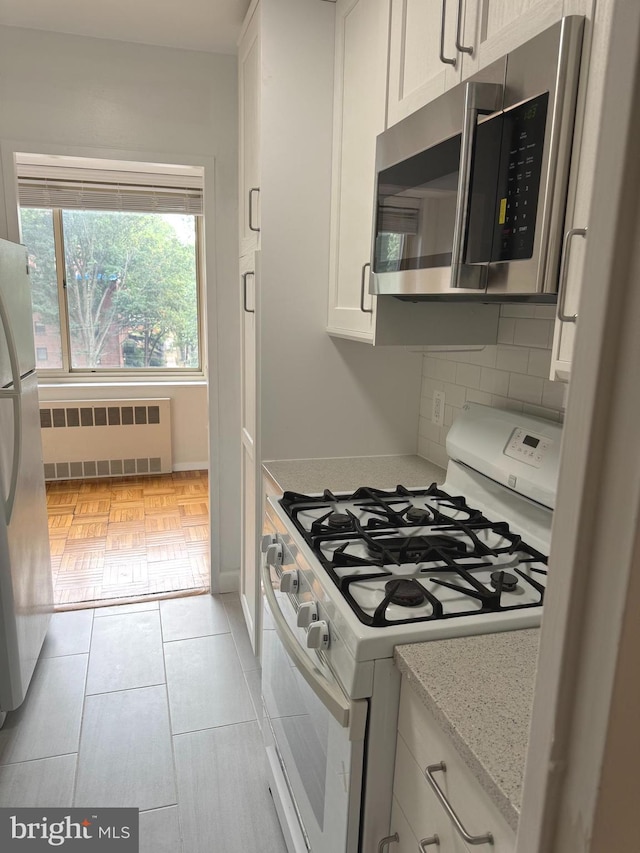 kitchen with tasteful backsplash, radiator heating unit, white cabinets, and stainless steel appliances