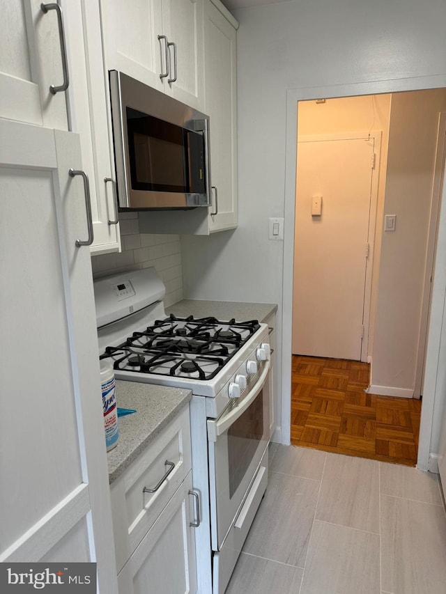 kitchen with gas range gas stove, white cabinets, decorative backsplash, and stainless steel microwave