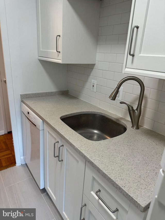 kitchen featuring white cabinetry, a sink, white dishwasher, and decorative backsplash