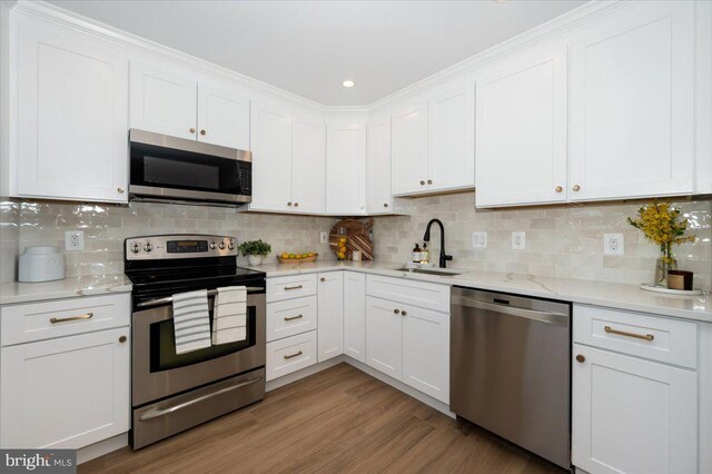 kitchen featuring stainless steel appliances, decorative backsplash, a sink, white cabinets, and wood finished floors
