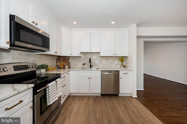 kitchen with white cabinetry, a sink, stainless steel appliances, and wood finished floors
