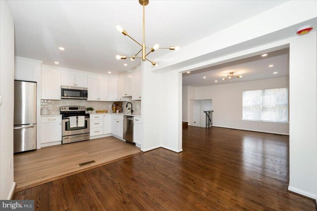 kitchen with visible vents, stainless steel appliances, a sink, open floor plan, and a notable chandelier