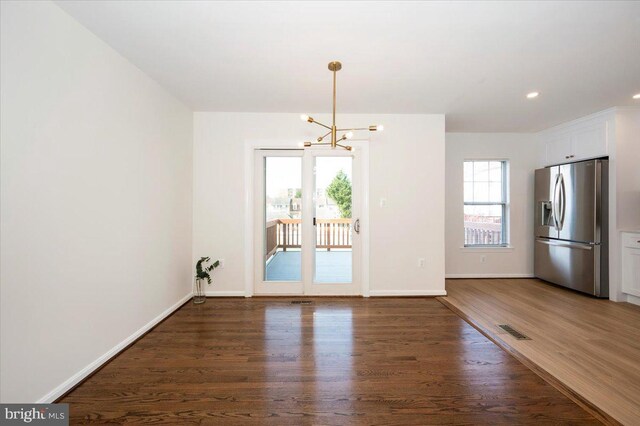 unfurnished dining area featuring wood finished floors, a notable chandelier, baseboards, and visible vents