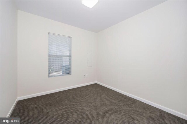 unfurnished room with baseboards and dark colored carpet