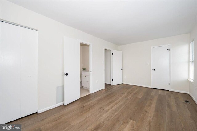 unfurnished bedroom featuring baseboards, visible vents, ensuite bathroom, and wood finished floors