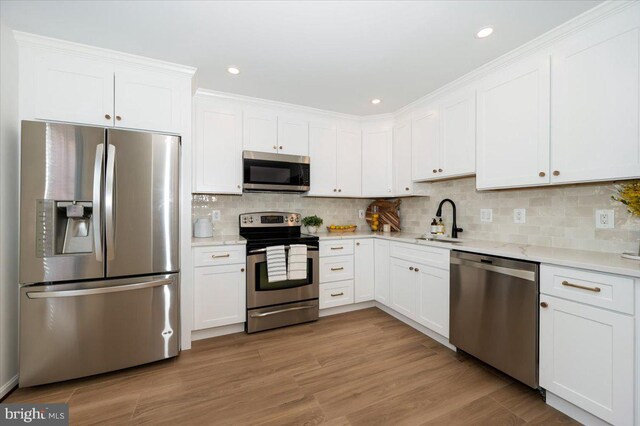 kitchen featuring decorative backsplash, stainless steel appliances, white cabinetry, a sink, and light wood-style floors