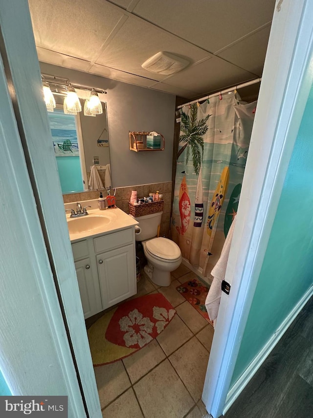 full bathroom featuring vanity, tile walls, a drop ceiling, tile patterned floors, and a wainscoted wall