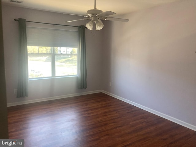 spare room featuring visible vents, baseboards, ceiling fan, and dark wood finished floors