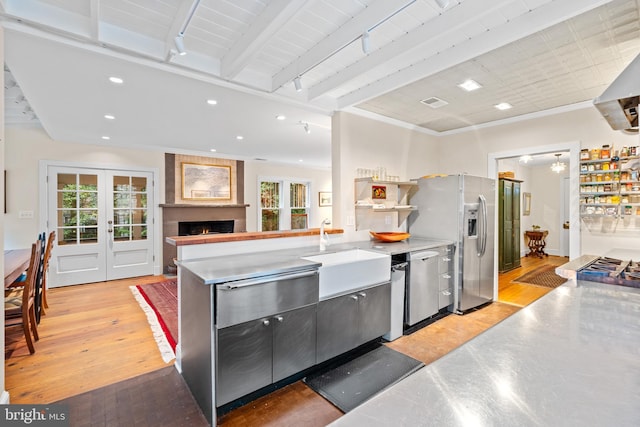 kitchen with a sink, stainless steel countertops, a fireplace, stainless steel appliances, and light wood-style flooring