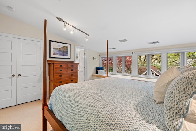 carpeted bedroom featuring rail lighting, a closet, vaulted ceiling, and visible vents
