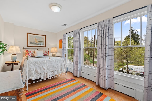 bedroom with a baseboard radiator, visible vents, multiple windows, and wood finished floors