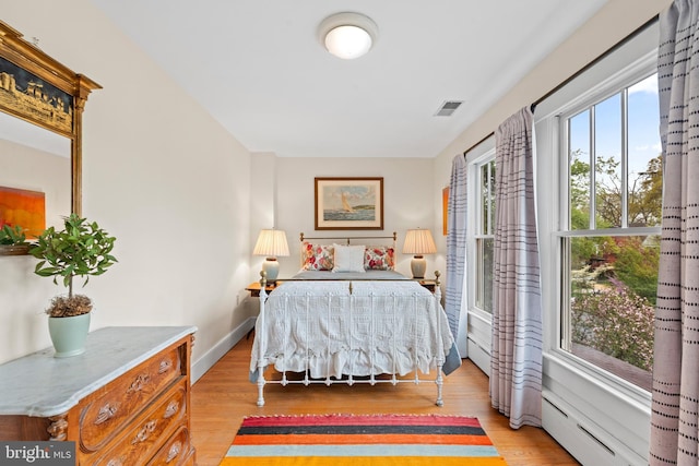bedroom with light wood-style floors, a baseboard heating unit, baseboards, and visible vents