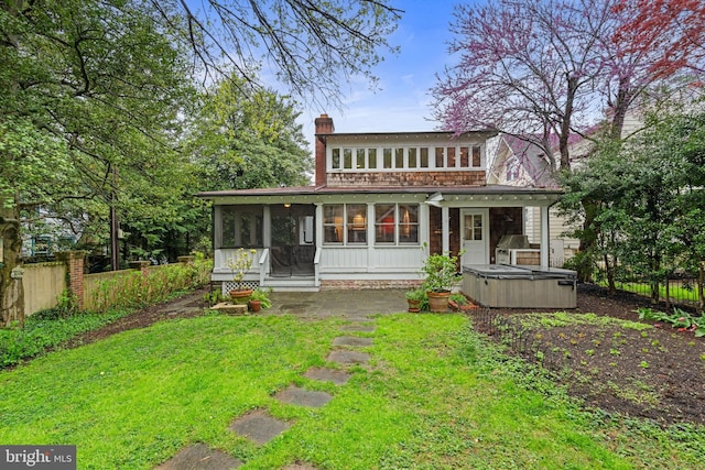 back of house with a hot tub, a sunroom, a lawn, fence, and a chimney