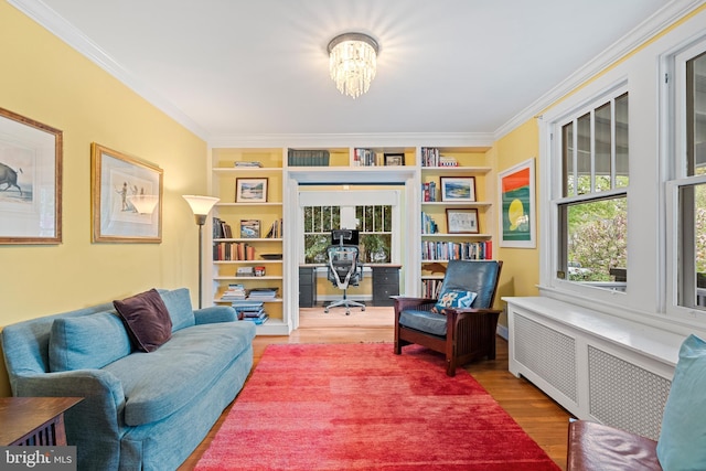 sitting room featuring built in shelves, ornamental molding, a chandelier, radiator, and wood finished floors
