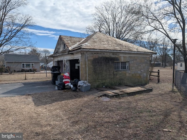 view of property exterior with an outdoor structure, concrete driveway, fence, and stone siding