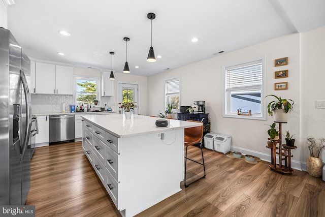kitchen with a kitchen breakfast bar, white cabinetry, wood finished floors, stainless steel appliances, and decorative backsplash