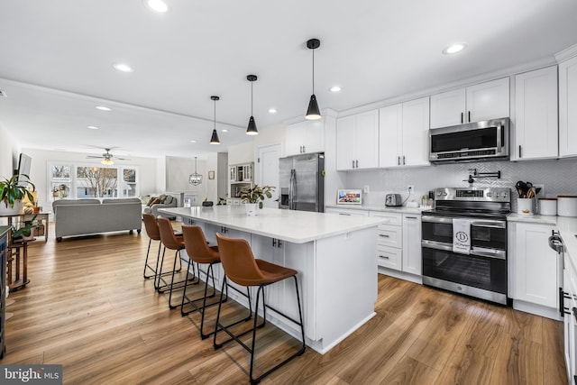kitchen with a kitchen bar, wood finished floors, ceiling fan, and stainless steel appliances