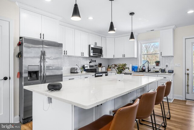 kitchen with white cabinets, appliances with stainless steel finishes, a breakfast bar, and light wood-style floors