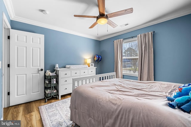 bedroom with crown molding, visible vents, a ceiling fan, and wood finished floors