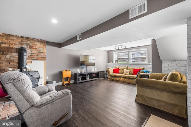 living room featuring brick wall, a wood stove, visible vents, and dark wood-style flooring