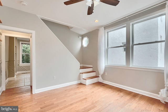 additional living space featuring stairs, ceiling fan, baseboards, light wood finished floors, and plenty of natural light