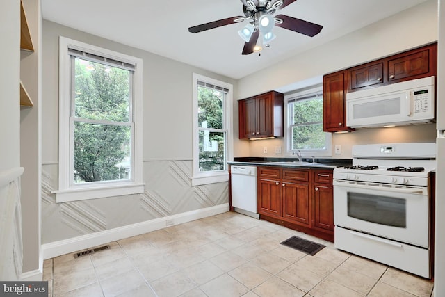 kitchen featuring white appliances, wainscoting, healthy amount of natural light, dark countertops, and a ceiling fan