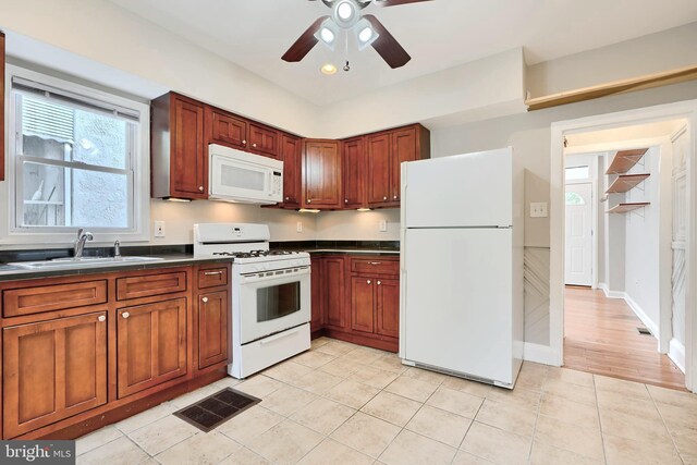 kitchen featuring white appliances, a sink, dark countertops, a ceiling fan, and light tile patterned flooring