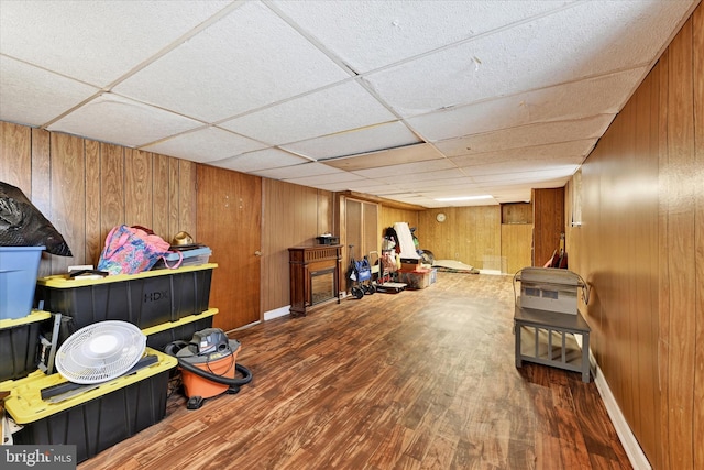 interior space featuring baseboards, wood finished floors, a paneled ceiling, and wood walls