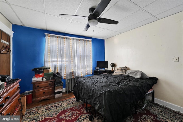 bedroom featuring baseboards, ceiling fan, a drop ceiling, and wood finished floors