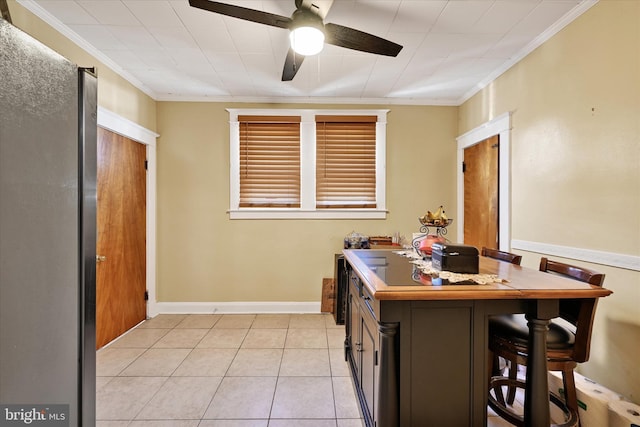 kitchen with crown molding, baseboards, ceiling fan, a kitchen breakfast bar, and light tile patterned floors