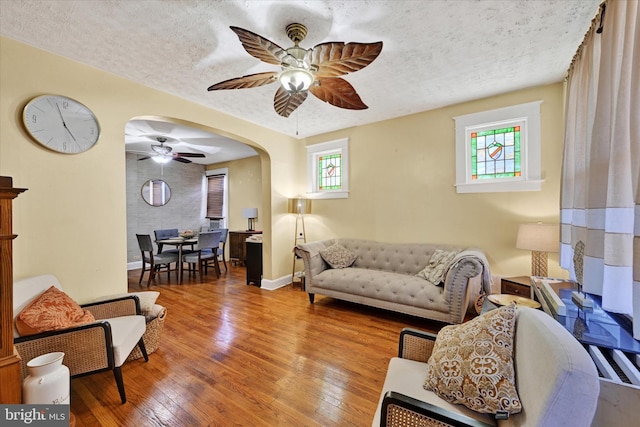 living room with a wealth of natural light, arched walkways, ceiling fan, and hardwood / wood-style floors