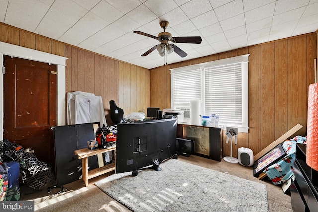 carpeted home office featuring ceiling fan and wood walls