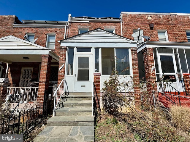 view of front of home with a sunroom, fence, and brick siding