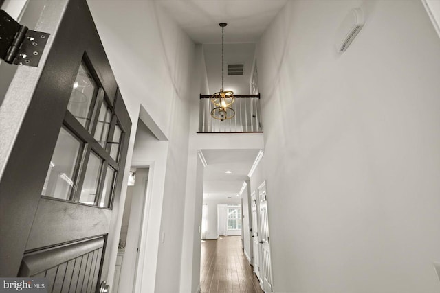corridor featuring visible vents, wood-type flooring, a notable chandelier, and a towering ceiling
