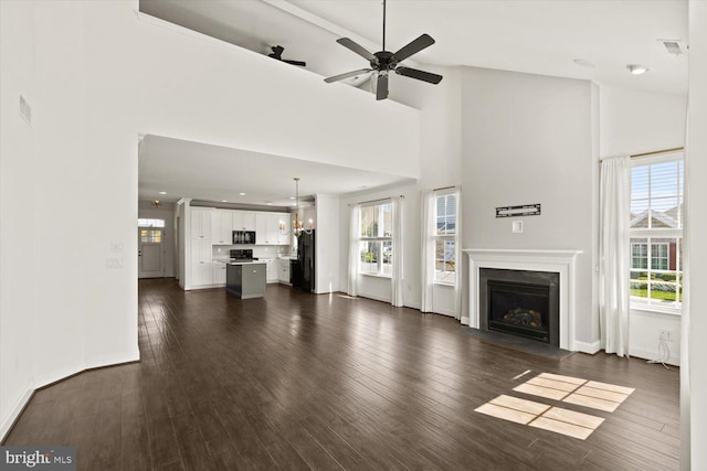 unfurnished living room with dark wood-style flooring, a fireplace with flush hearth, plenty of natural light, and a towering ceiling
