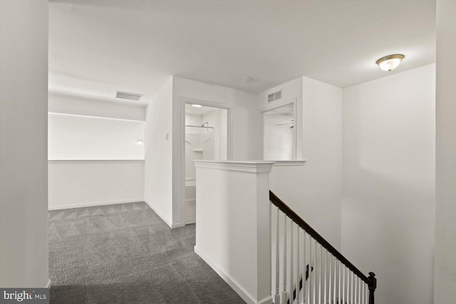 hall featuring carpet floors, visible vents, and an upstairs landing