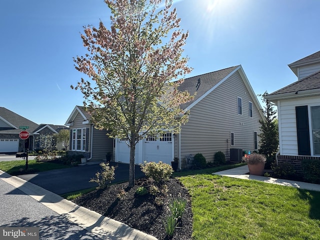 view of side of property with a lawn, a garage, driveway, and cooling unit