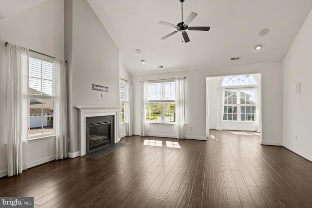 unfurnished living room featuring visible vents, a glass covered fireplace, ceiling fan, dark wood-style floors, and high vaulted ceiling